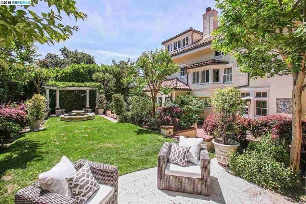This view of the backyard patio showcases the beautiful pair of woven wicker sofas on a concrete floor that stops on the edge of the grass lawn that leads to the fountain on the far side.