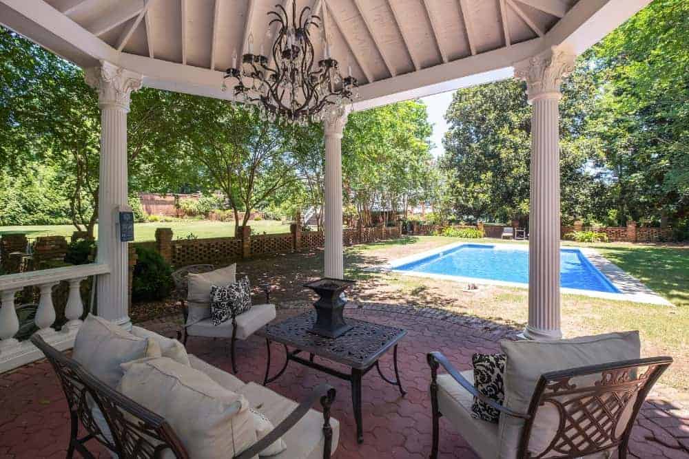 This is the elegant covered patio that has a majestic chendelier hanging over the outdoor sofa set on the terracotta brick flooring. This transitions to a grass lawn before reaching the pool area.