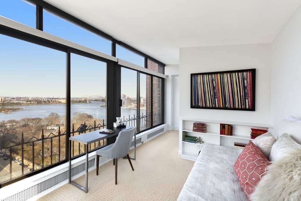 The white walls and ceiling of this home office is brightened by the natural lighting coming in from the glass walls. These are then contrasted by the black elements of the window frames, desk and artwork frames.
