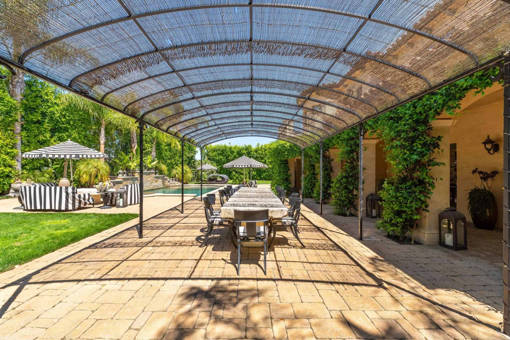 This is a large foyer with stone brick flooring and walkway leading to the grass lawn and the pool side on the far side. This area is topped with a lovely canopy that gives shade to the outdoor dining area.