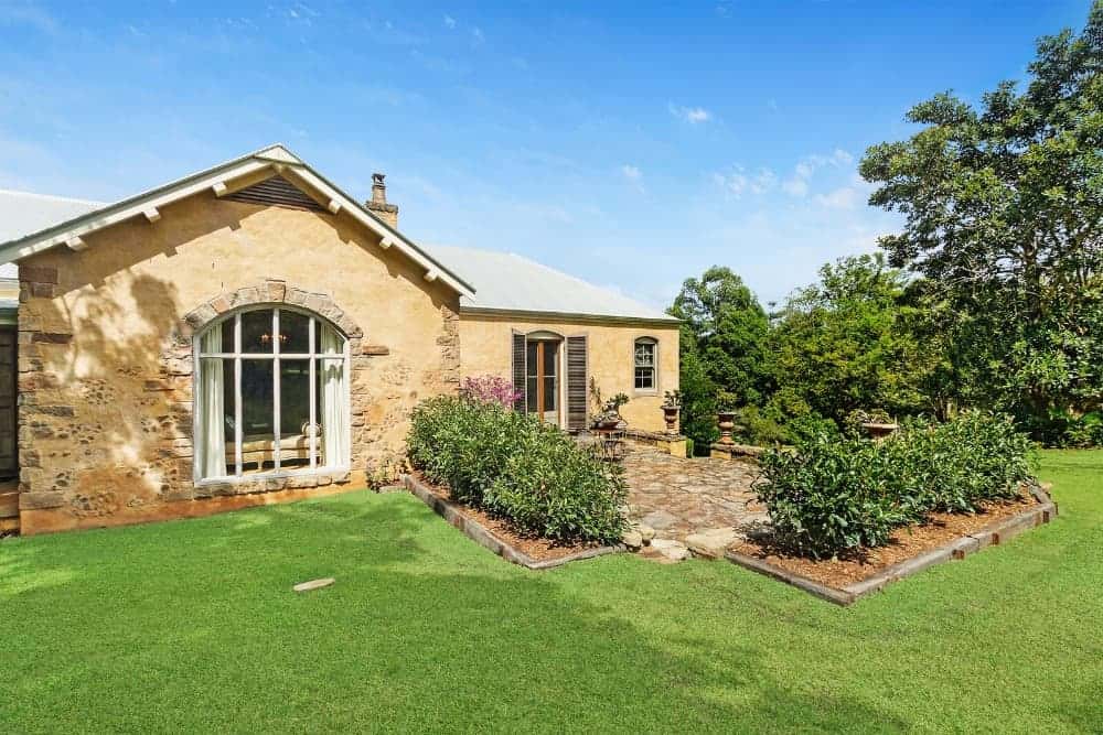 This is a look at the backyard patio that has mosaic stone flooring bordered by gorgeous planters filled with shrubs before transitioning to the grass lawn.