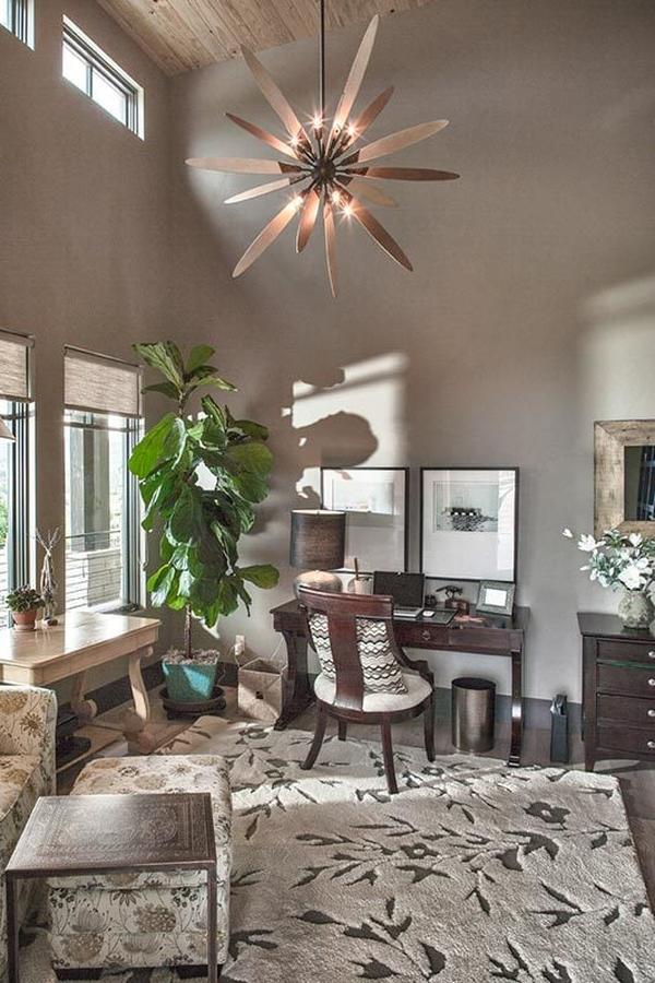 The study has a dark wood desk, floral area rug, and a statement chandelier hanging from the high vaulted ceiling.