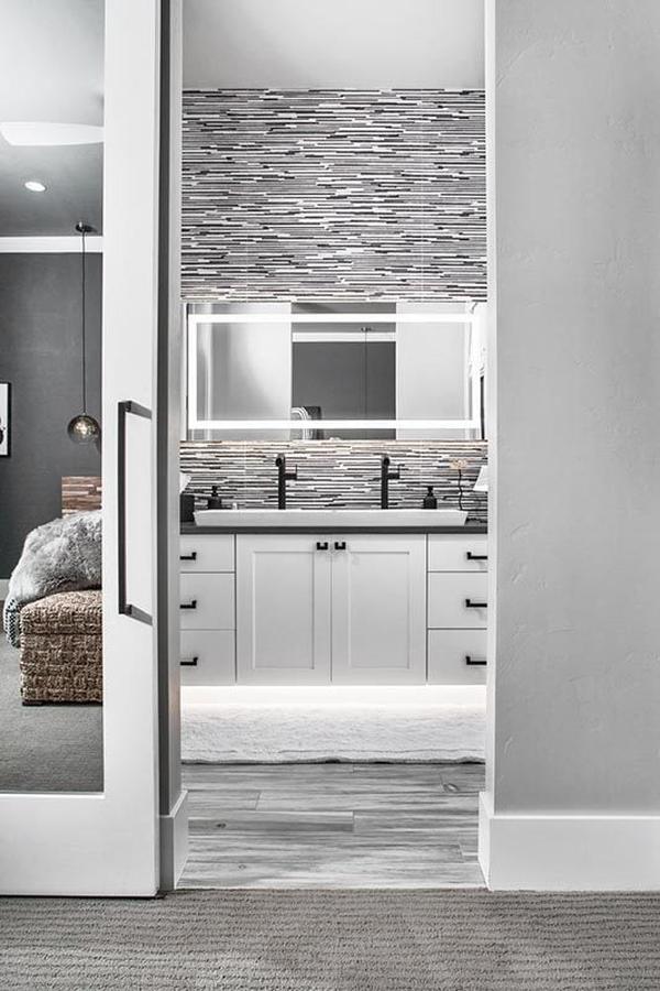 A sliding glass door opens to the bathroom with an illuminating mirror and white sink vanity contrasted with wrought iron fixtures and hardware.