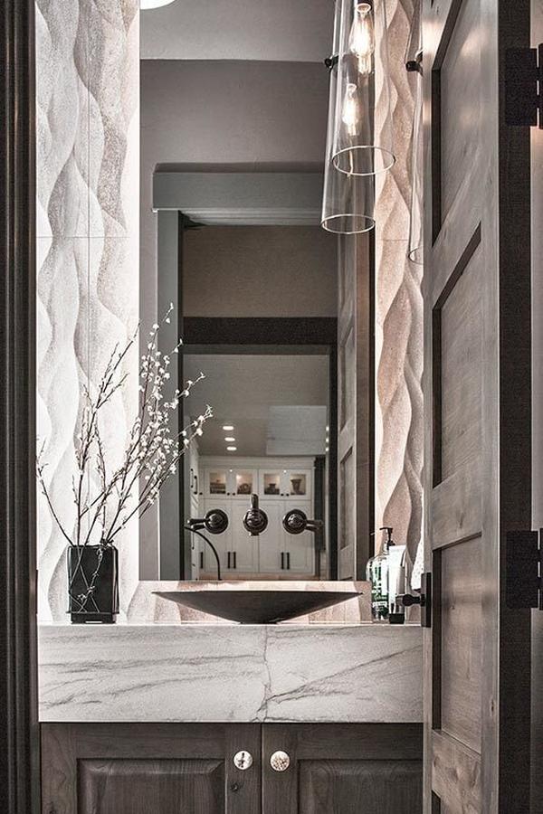 A powder room with glass sconces and a vessel sink vanity crowned with a white marble countertop.