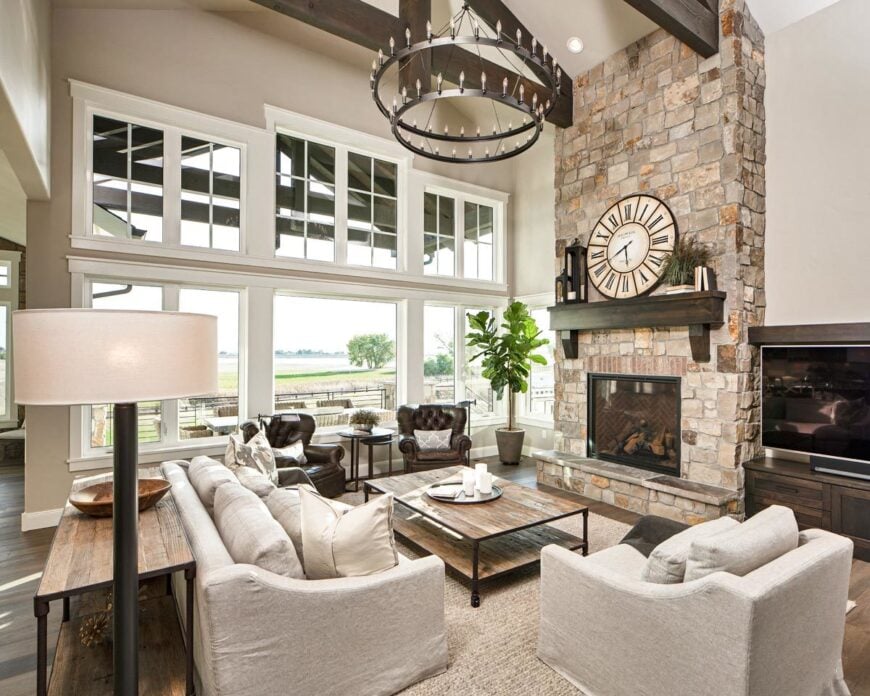 The living room offers gray upholstered seats, a rustic coffee table, and a stone fireplace with a round clock on top.