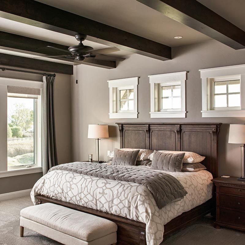 Primary bedroom with carpet flooring and a regular taupe ceiling lined with dark wood beams.