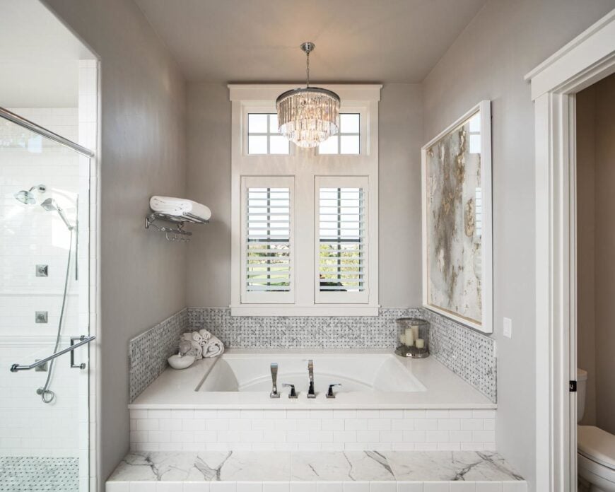 The primary bath is equipped with a water closet, a walk-in shower, and a deep soaking tub under the round crystal chandelier.