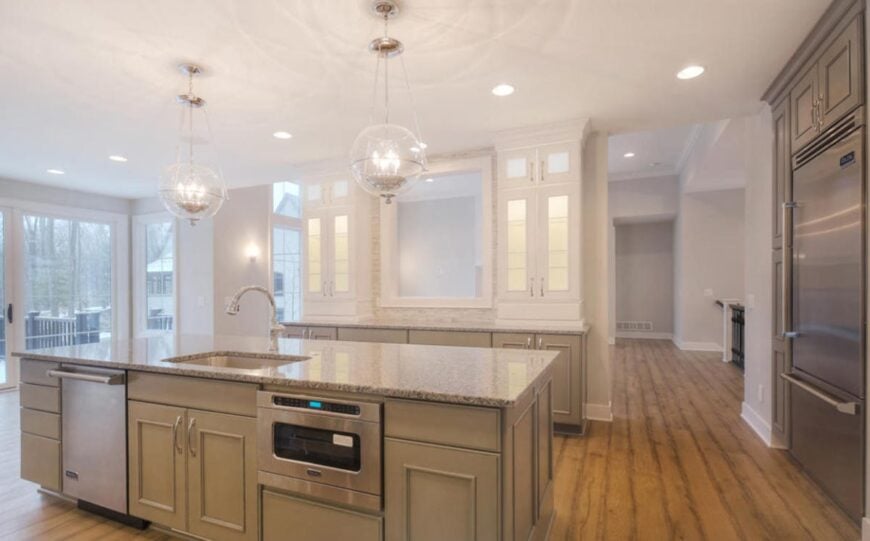 The kitchen has rustic hardwood flooring and a regular white ceiling mounted with recessed lights and a pair of glass globe pendants.
