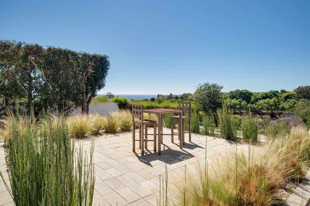 This is the lovely backyard patio of the house fitted with an intimate outdoor dining set in the middle of a concrete brick floor that is surrounded by planters with decorative shrubs.