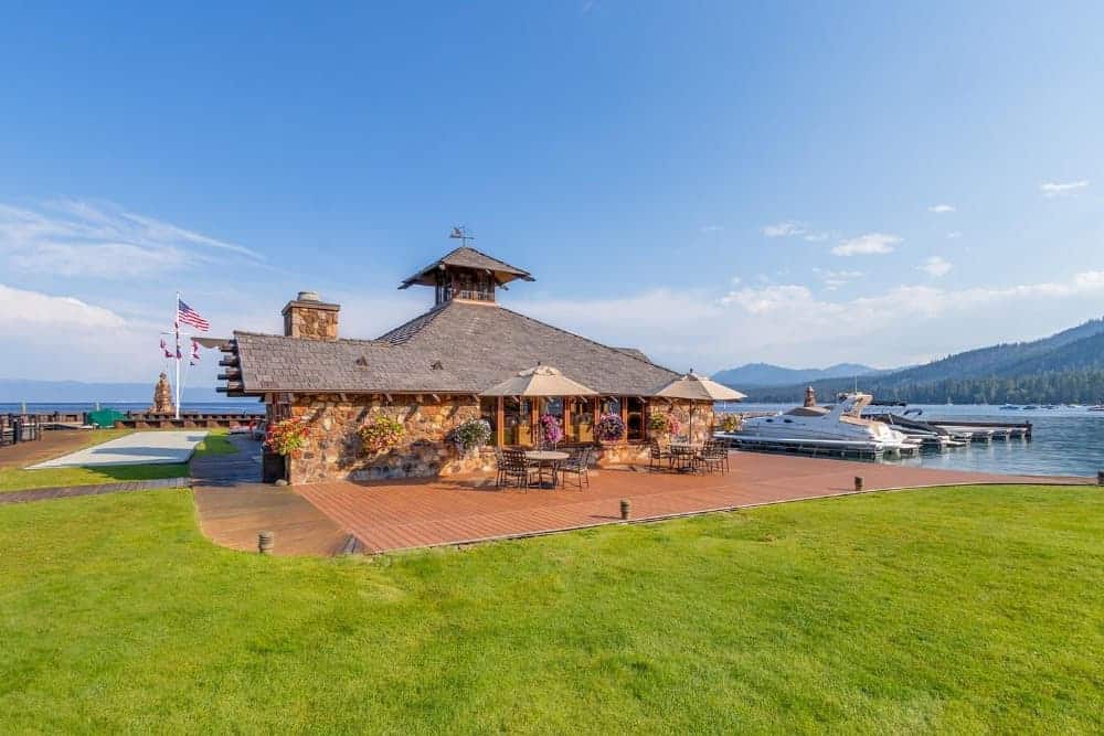 This is the view of the backyard patio fitted with a charming outdoor dining area. This patio has a wooden flooring surrounded by outdoor lighting before it transitions to the well-maintained grass lawn.