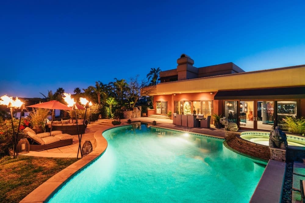 This is the view of the back of the house with concrete walkways surrounding the large pool. These areas are fitted with an outdoor dining area and sitting areas lit by outdoor torches.