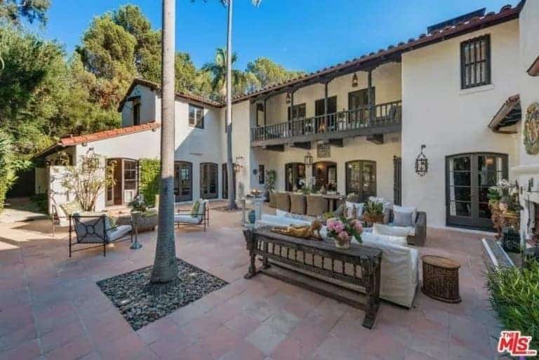 This is the gorgeous spacious patio with sitting areas and an outdoor dining area all on terracotta flooring outdoor tiles that go well with the beige exterior walls of the house. Here you can also see the tropical trees on pebbled soil framed by the outdoor tiles.