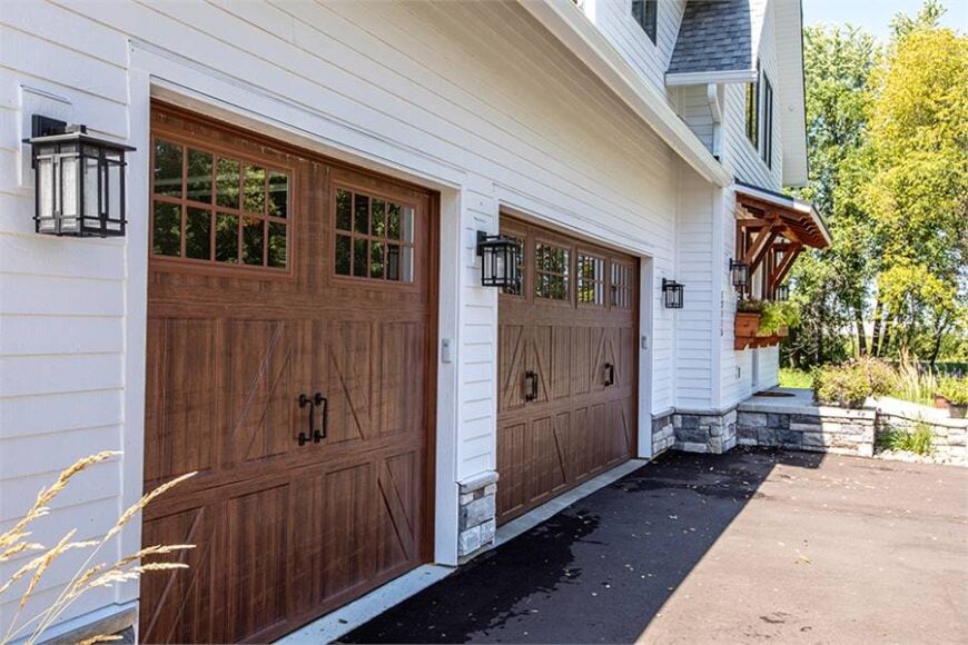 A close-up look at the garage with large wooden doors illuminated with outdoor sconces.