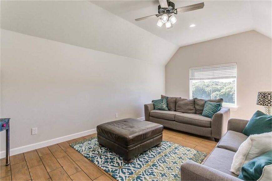A living space with a vaulted ceiling and a wide plank flooring topped by a patterned area rug.