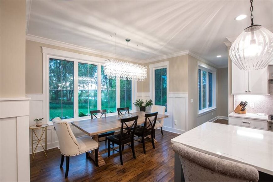 The dining area sits adjacent to the kitchen. It offers a rectangular dining set illuminated with a linear glass chandelier.