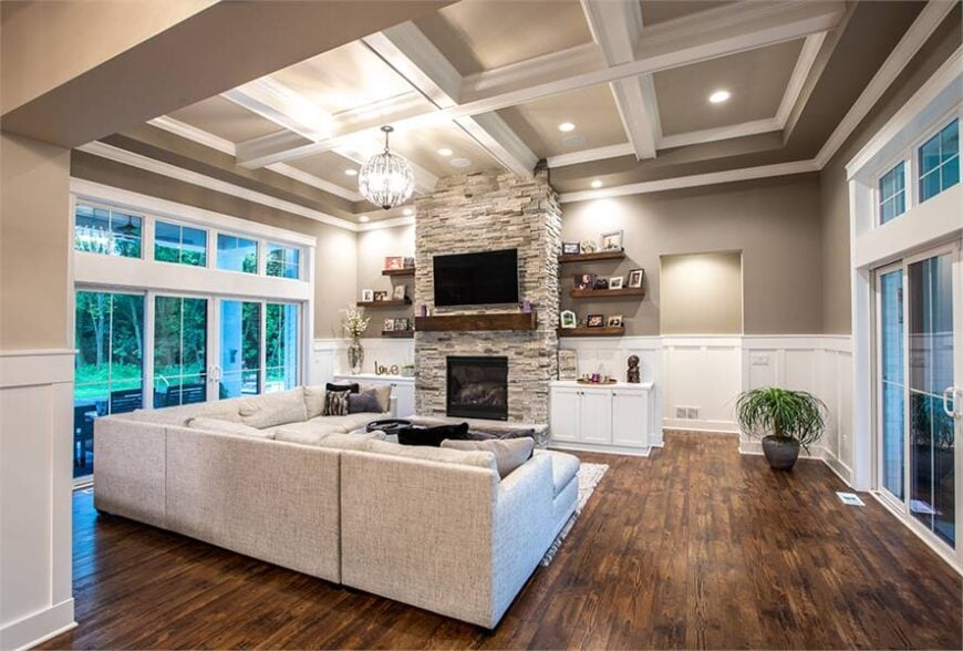 The living room has natural hardwood flooring and a stunning coffered ceiling mounted with recessed lights and a round chandelier.