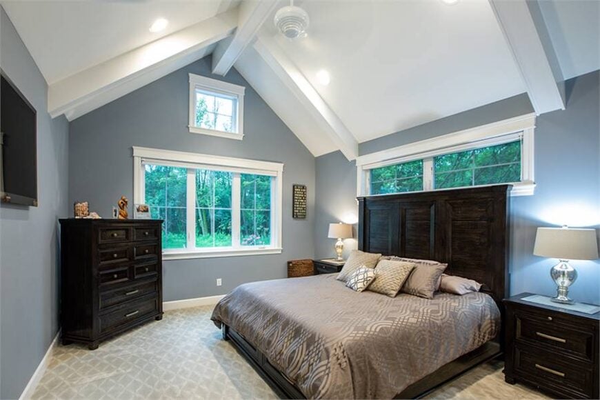 Primary bedroom with a beamed cathedral ceiling and light blue walls fitted with white framed windows.