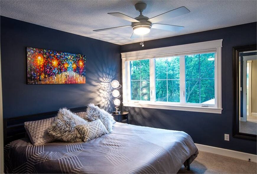 This bedroom is decorated with fancy table lamps, furry pillows, and a bold artwork mounted on the dark blue wall.