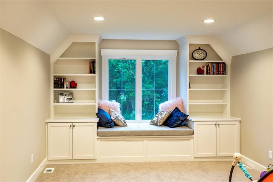 A loft with window seat flanked by white built-ins. It is topped with a beige cushion and various pillows.