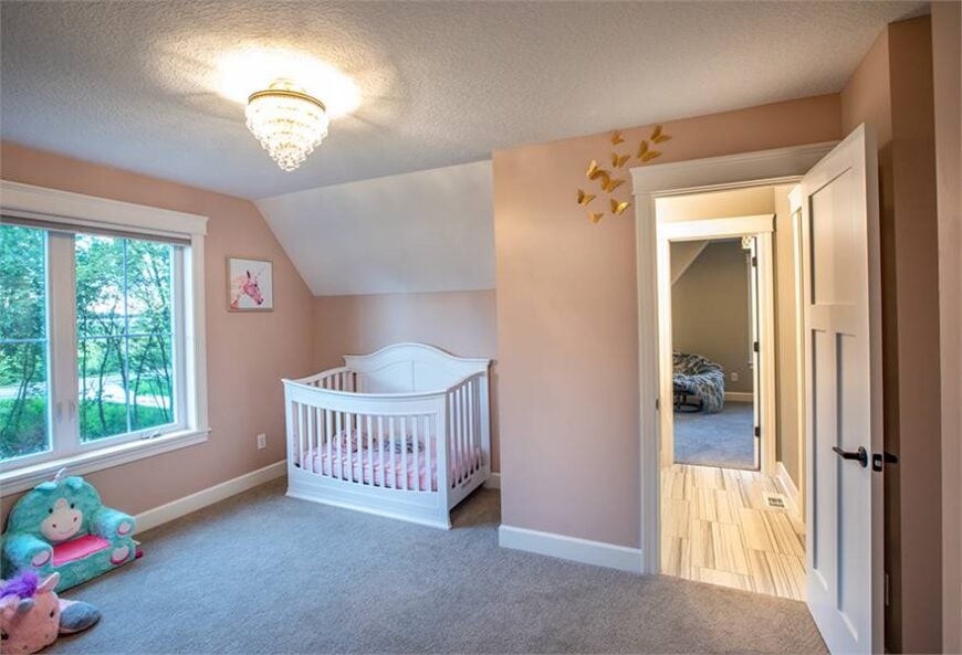 Nursery room with light pink walls and a vaulted ceiling mounted with a warm semi-flush light.