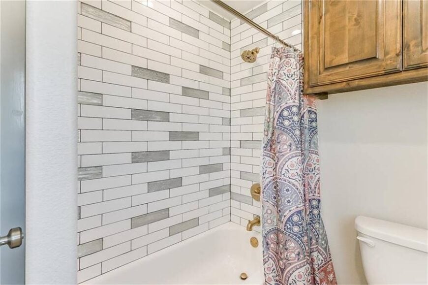 The shower and tub combo next to the toilet is complemented with brass fixtures and a lovely printed curtain that serves as its door.