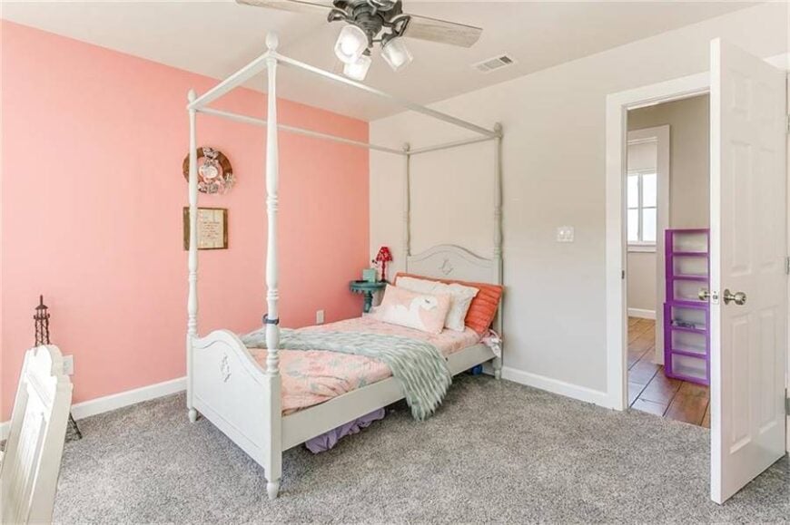 Kid's bedroom with dual-tone walls and a canopy bed sitting on a gray carpet flooring.