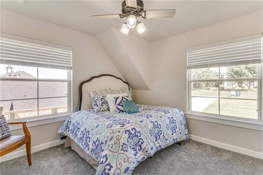 A smaller bedroom furnished with a wooden chair and a beige upholstered bed that's covered in an oversized patterned duvet.