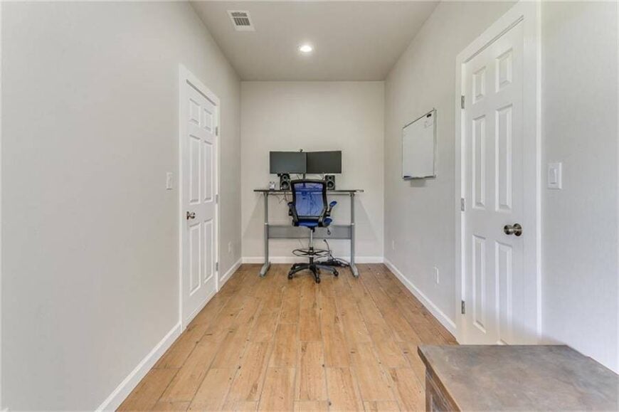 The home office has a sleek desk and a blue swivel chair sitting on a wide plank flooring.