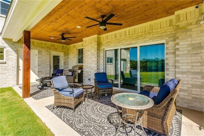 The covered lanai is furnished with large patterned rugs, metal round tables, and armchairs topped with blue cushions.