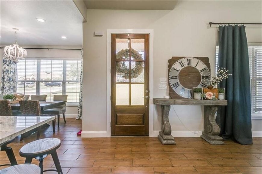 Foyer with a wooden front door and a classic console table topped with small potted plants and a large clock.