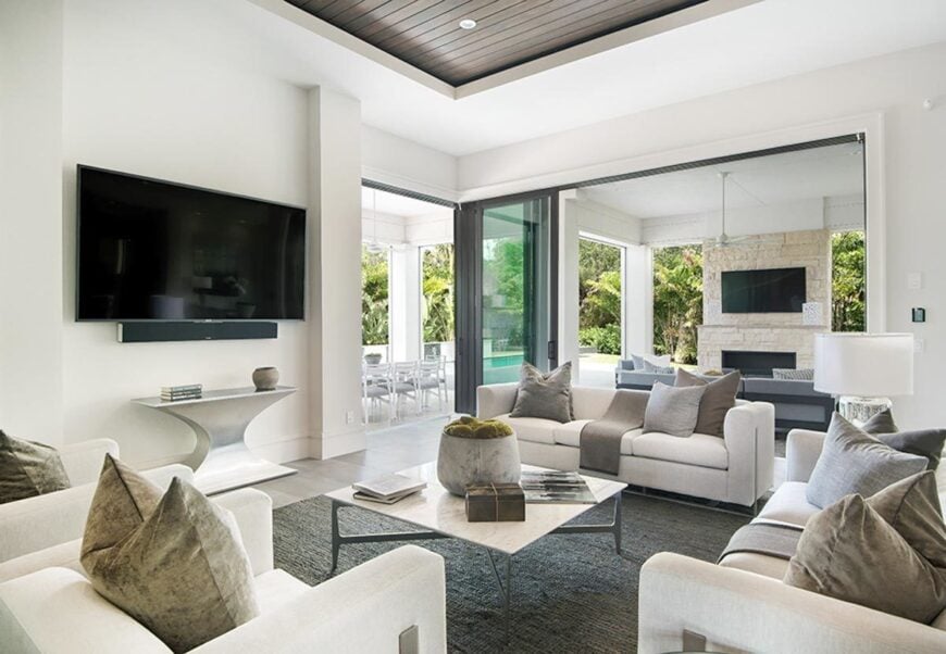The living room has sleek light gray seats and a metal coffee table facing the wall-mounted TV fixed above the modern console table.