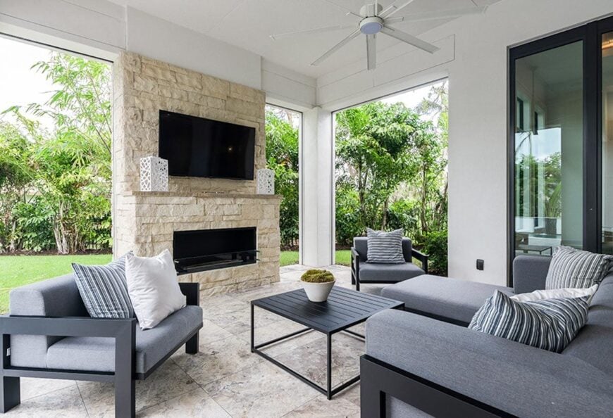 The outdoor living offers cushioned seats, a metal coffee table, and a brick fireplace with a TV on top.