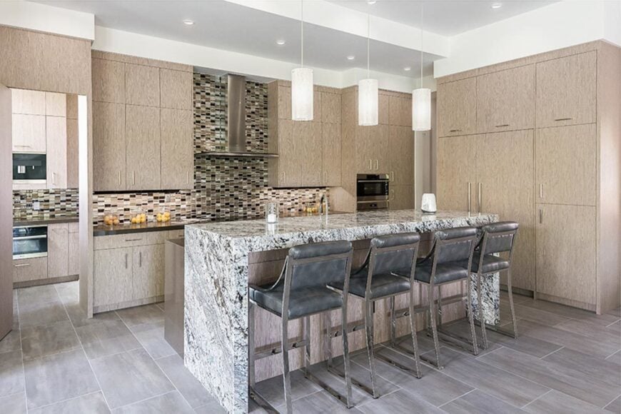 The kitchen has a two-tier island and light wood cabinets accented with a linear mosaic tile backsplash.