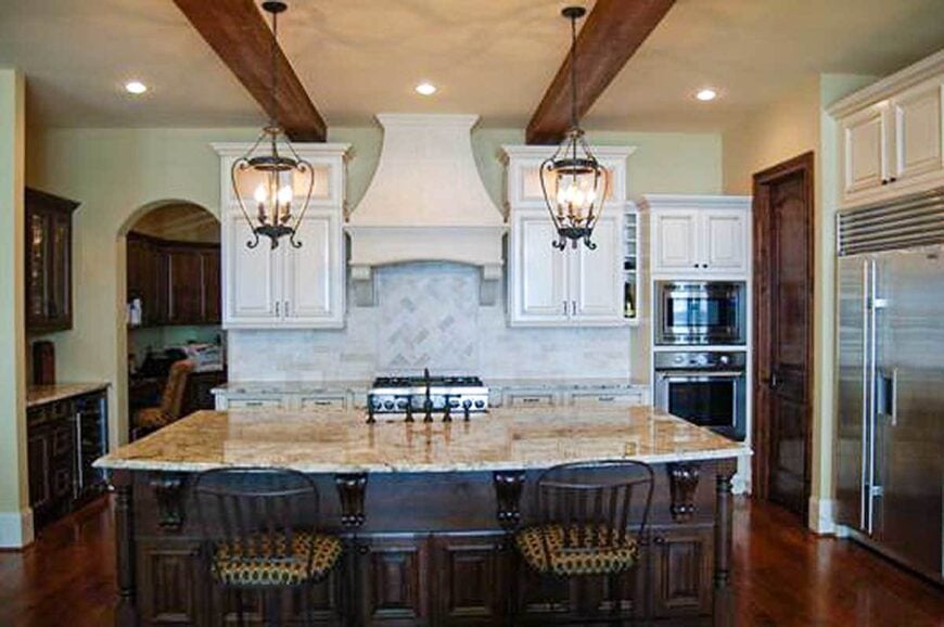 The kitchen offers stainless steel appliances, white cabinets, and a large island bar complemented with cushioned counter chairs and warm pendant lights.