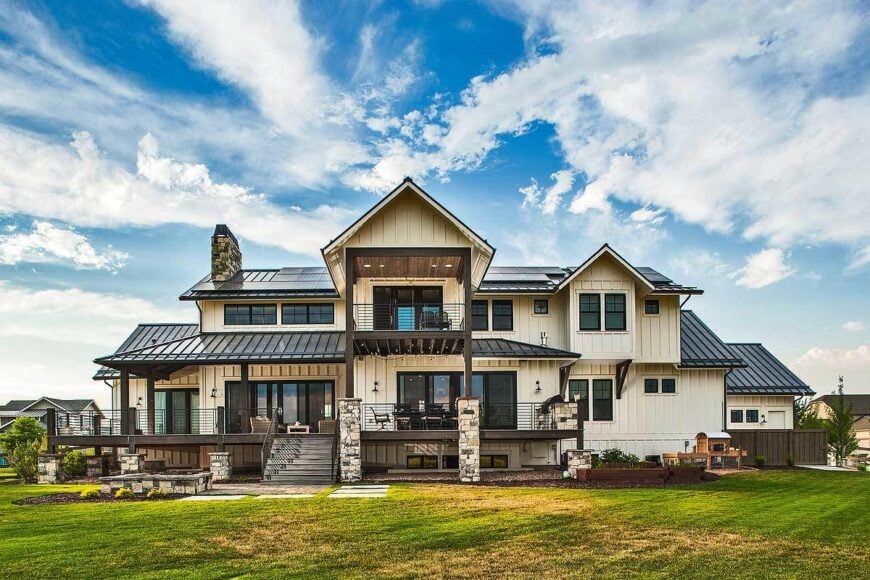 View of the house from the backyard showing the white board and batten siding along with a covered deck that's framed with wrought iron railings and dark wood posts.