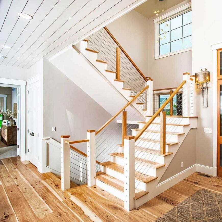 The foyer features a traditional staircase with metal railings and wooden steps that match the wide plank flooring.