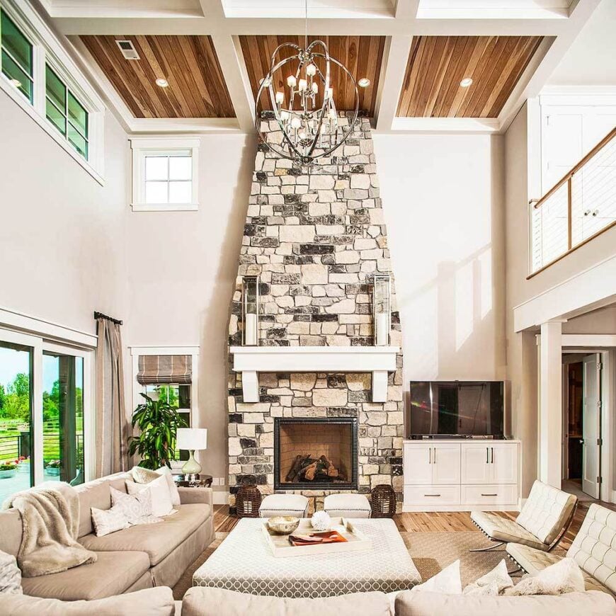 The living room has a stone fireplace, cozy beige seats, and a spherical chandelier that hangs from the high coffered ceiling.