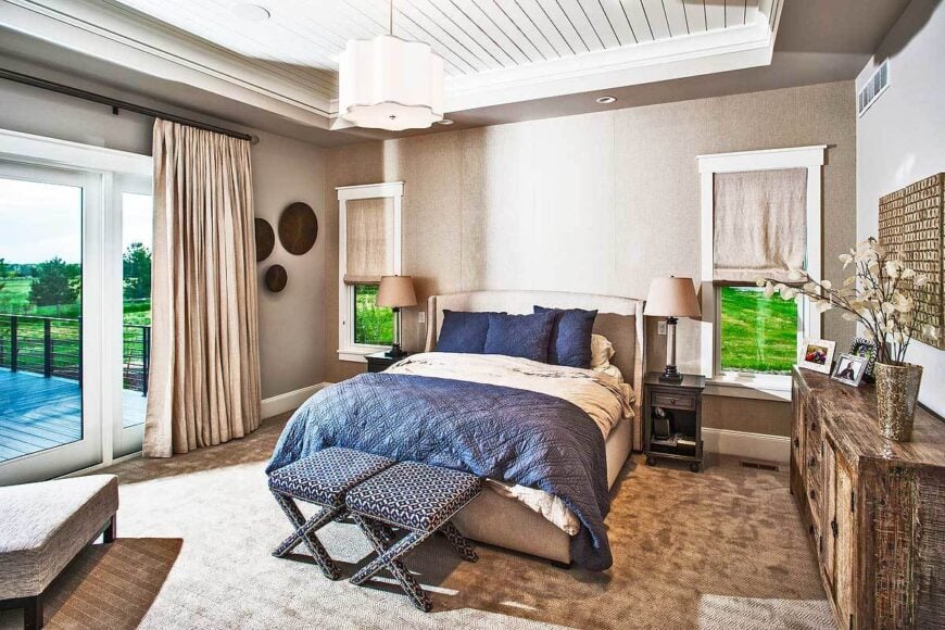 The primary bedroom features a beige upholstered bed flanked by small wooden nightstands and white framed windows.