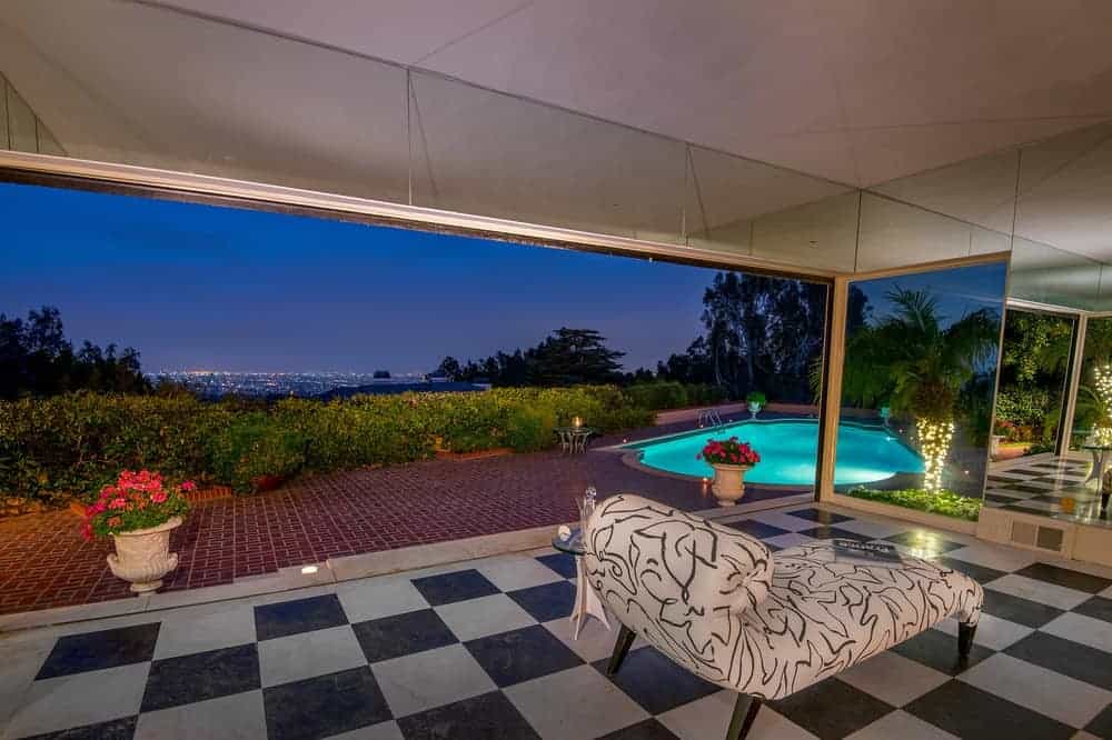 This is the covered patio with a lovely black and white flooring that transitions to terracotta brick outdoor walkway that leads to the surrounding shrubs and the poolside area.