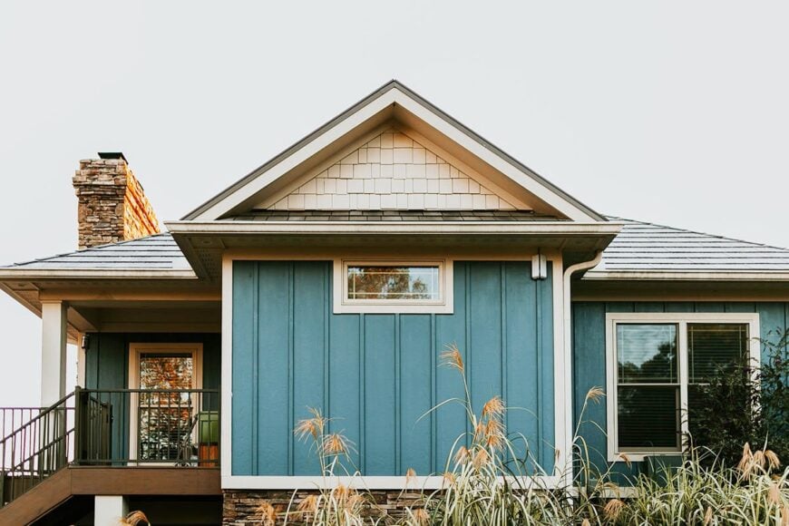 Hipped and center gable roofs top the bungalow house with vertical exterior siding and covered deck.