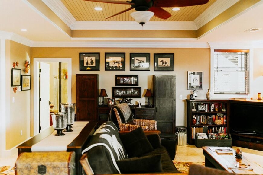 Another living room filled with dark wood furnishings, black-framed artworks, and a tray ceiling mounted with a fan and recessed lights.