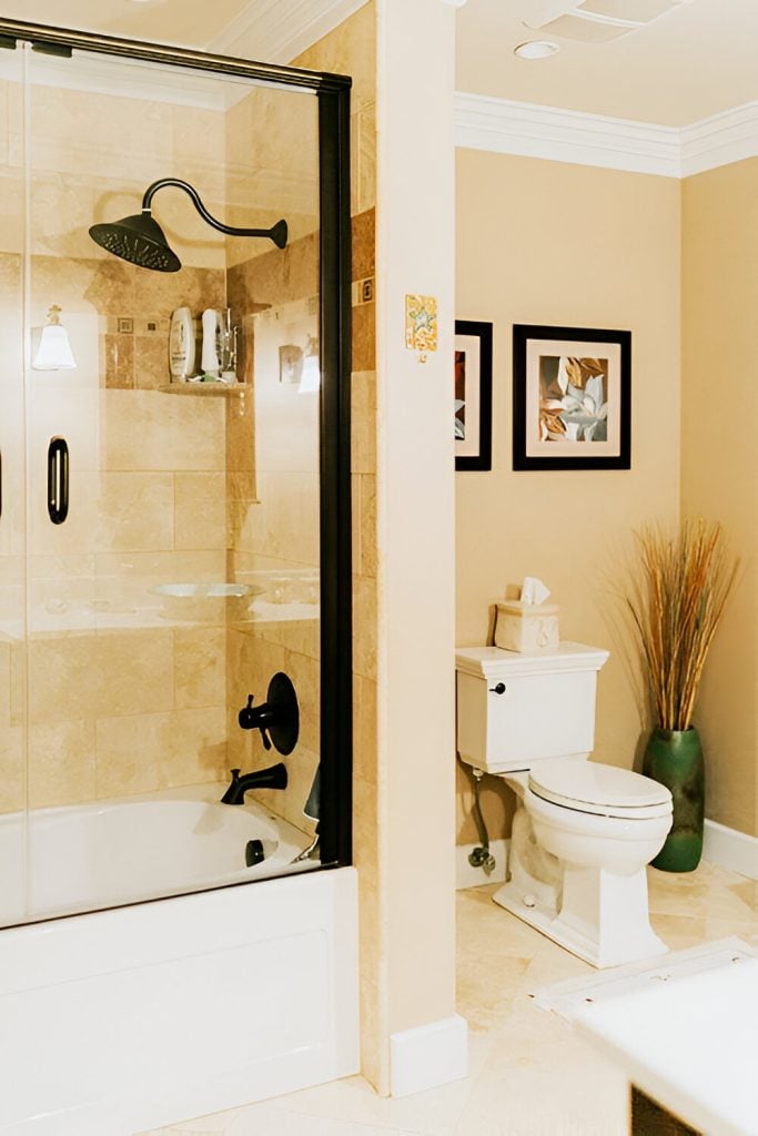 This bathroom is equipped with a toilet and a shower and tub combo fitted with wrought iron fixtures.