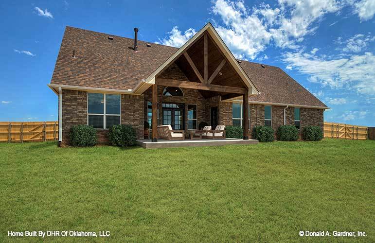 View of the home from the backyard showing a covered porch framed with rustic wooden trims and columns.