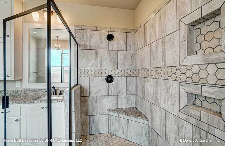 The walk-in shower has hex tile flooring, a corner tiled bench, and inset shelves fitted on the marble-tiled walls.