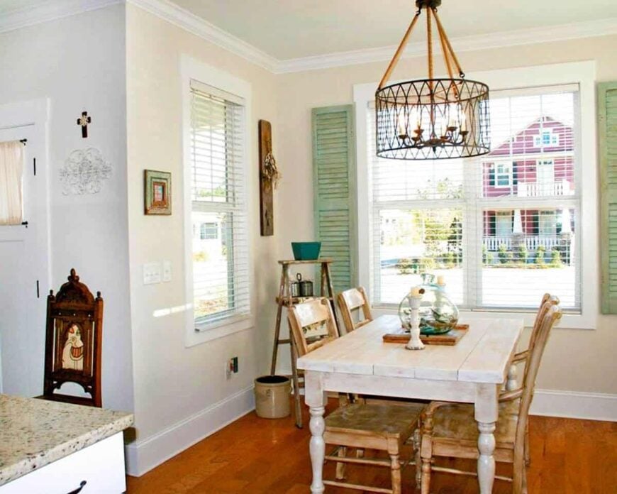 Dining area with rustic wooden chairs and a white distressed dining table illuminated with a drum chandelier.