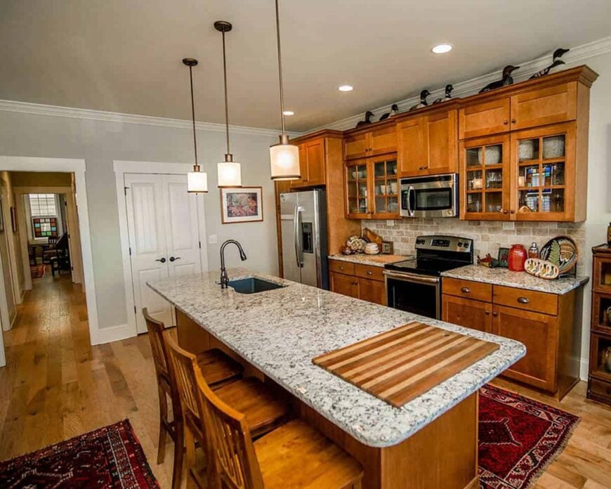 The kitchen has granite countertops, wooden cabinets, and an island bar fitted with an undermount sink.