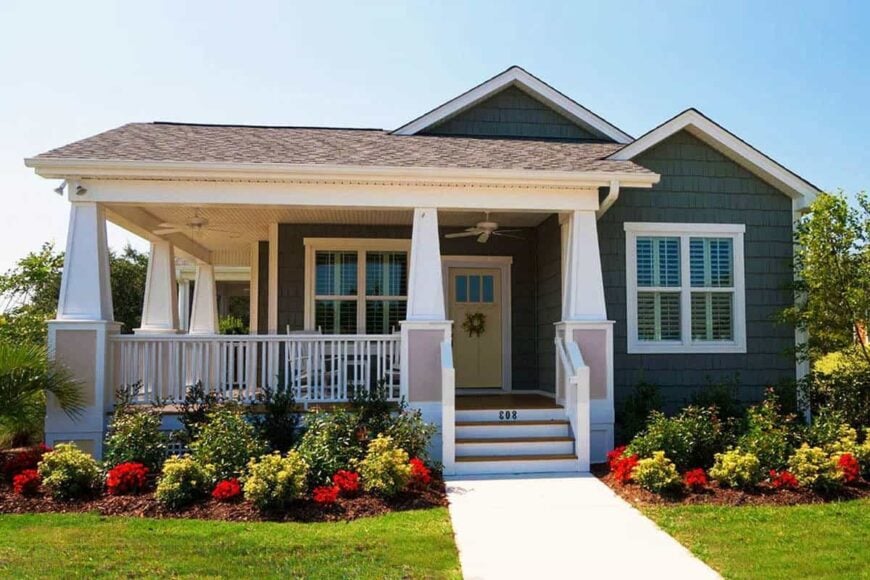 Home's exterior view showing the dark green siding, a wooden stoop, and a wrap-around porch supported by tapered columns.