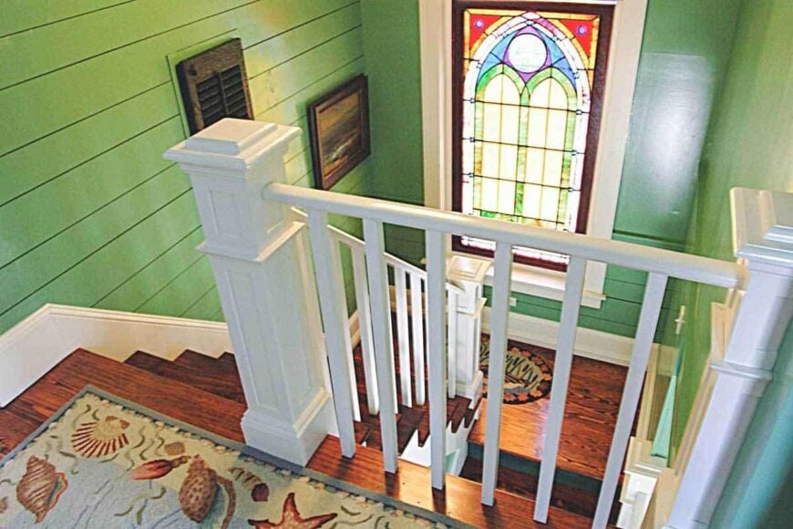 View of the staircase landing from the second floor boasting a stained glass window that lets natural light in.