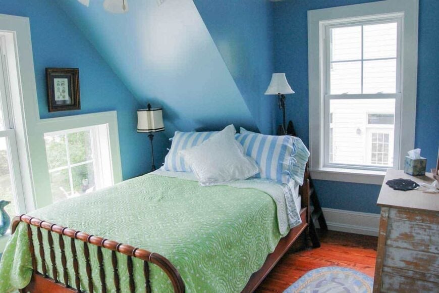 This bedroom offers a cozy wooden bed, distressed dresser, and an oval rug that lays on the red hardwood flooring.