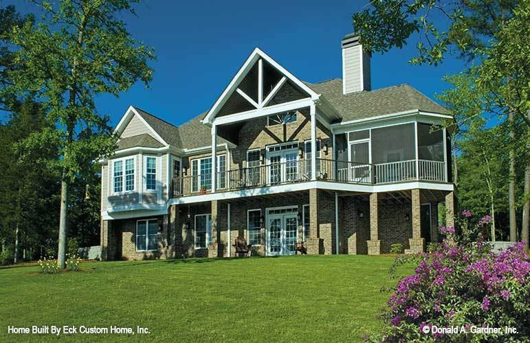 Rear exterior view showing the screened porch, wide deck, and expansive porch framed with stone columns.
